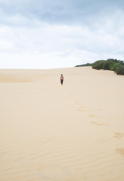 Vertical ImageRear View of Young Man Walking on a Sand Dune in a Sunny DayExploration Concept