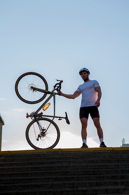 Vertical low angle shot of a handsome athletic male cyclist and his bike outdoors on hot summer day