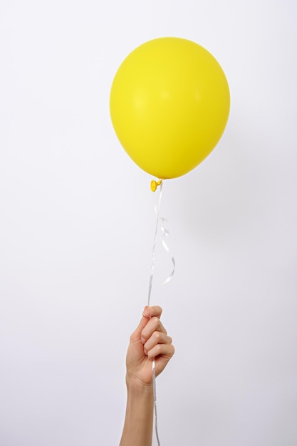 Vertical one minimal yellow balloon in hand on white background copy space element of decorations for birthday party wedding festival