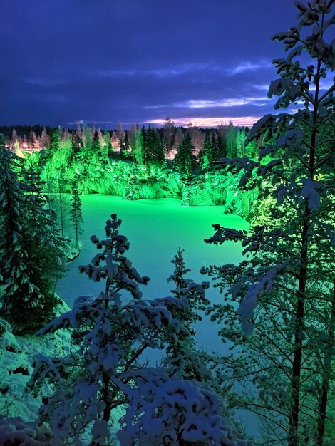 Vertical photo of beautiful place marble canyon in Republic of Karelia with colorful lights in snow at night in winter snowy day. Ruskeala, Sortavala