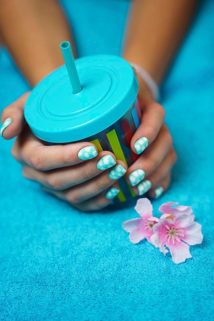 Vertical photo of beautiful women's hands with colored manicure and a multicolored cup with a drinking tube