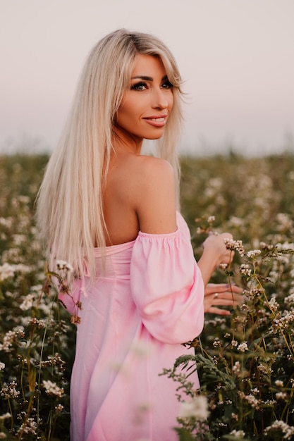 Vertical photo blonde woman posing in the big endless field of daisies in summer evening