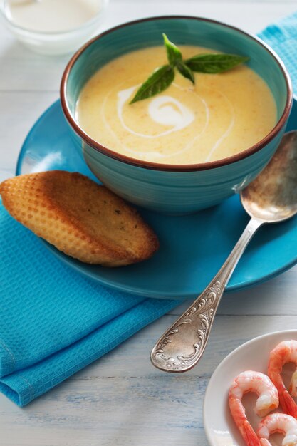 Photo vertical photo of bowl of cream soup with shrimps, basil and bread