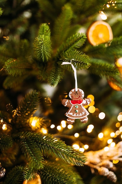 Vertical photo of gingerbread cookie in the shape of a man weighs on a Christmas tree with bokeh lights decoration.