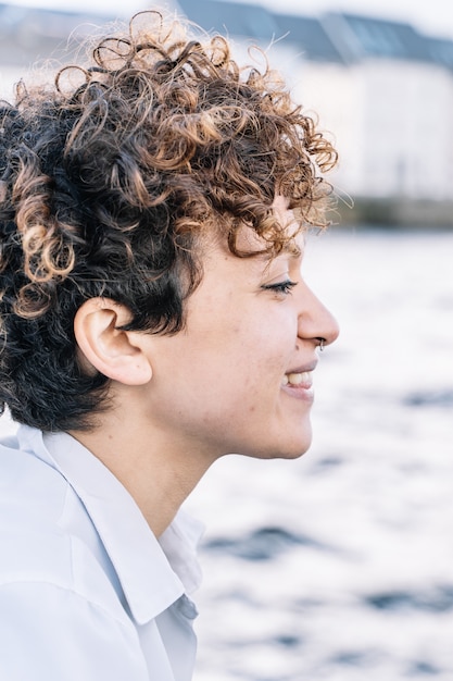 Vertical photo of a girl in profile with curly hair and a piercing  nose looking in front