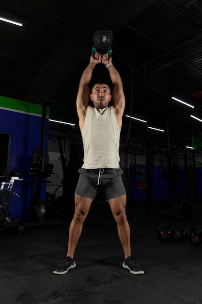 Vertical photo of a latin man exercising with a kettlebell in a gym standing up