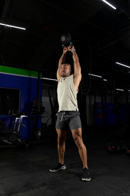 Vertical photo of a latin man exercising with a kettlebell in a gym standing up