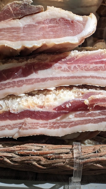 Vertical photo of a lot of thick pieces of pork bacon in a basket at a market in Portugal