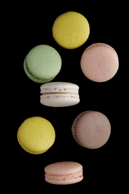 Vertical photo of macaroon. Colorful cake macaron with pastel tones in chaotic levitation on black wall. Top view of almond cookies.