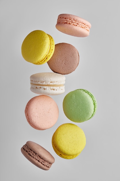 Vertical photo of macaroon. Colorful cake macaron with pastel tones in chaotic levitation on gray wall. Top view of almond cookies.