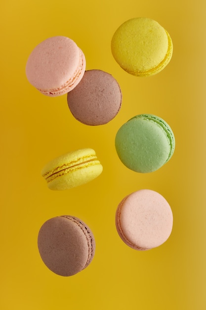 Vertical photo of macaroon. Colorful cake macaron with pastel tones in chaotic levitation on yellow surface Top view of almond cookies.