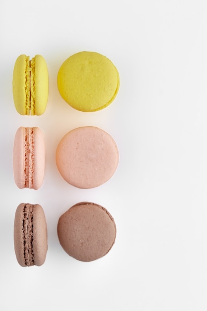 Vertical photo of macaroon. Six colorful cakes macaron with pastel tones lay and stand straight on white surface. Top view of almond cookies.