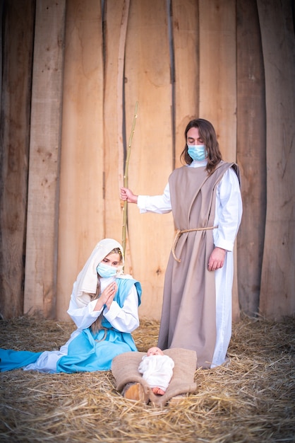 Vertical photo of a nativity scene with the characters wearing masks while adoring Jesus baby