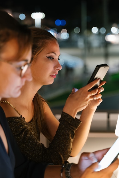 Vertical photo of a women sitting on a terrace at night while using the mobile