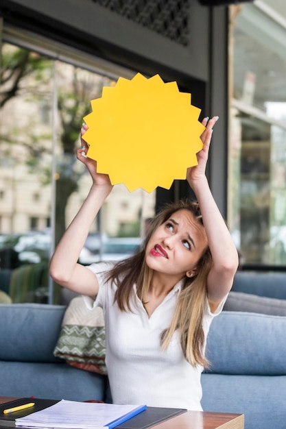 Vertical photo of young blonde holding idea board top of her head and looking at it