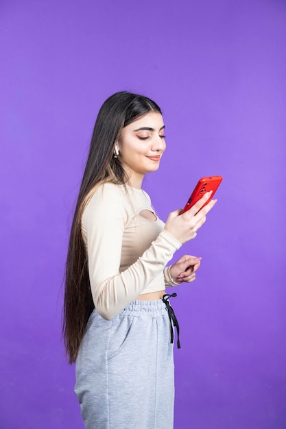 Vertical photo of young lady holding phone and stands on purple background