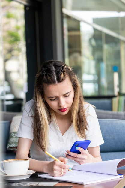 Vertical photo of young lady looking at her phone and writing notes