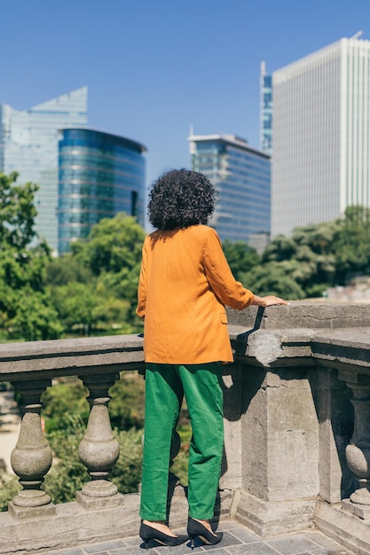 Vertical photograph of fashionable lady from behind in jacket pants and heels looking at city skyscrapers