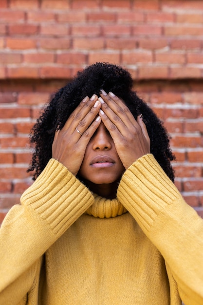 Vertical portrait of African American woman covering eyes with hands Fear concept