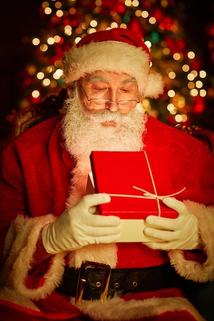 Vertical portrait of bearded traditional santa claus opening present with light inside by christmas