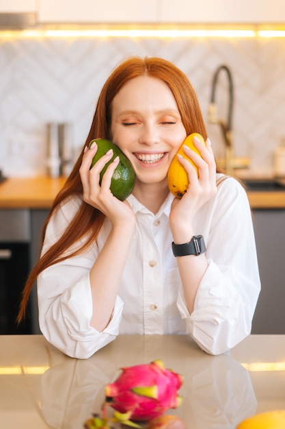 Vertical portrait of cheerful attractive redhead young woman holding in hands mango and avocado