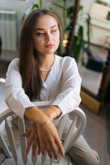 Vertical portrait of confident businesswoman sitting on chair with legs wide open and holding hands on back of chair looking away