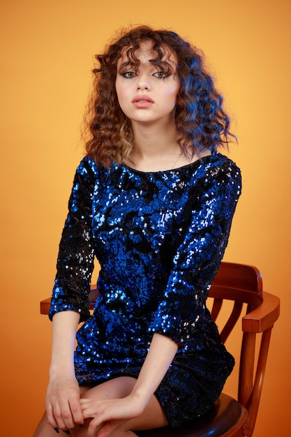 Vertical portrait of curlyhaired girl sitting on a chair on orange background High quality photo