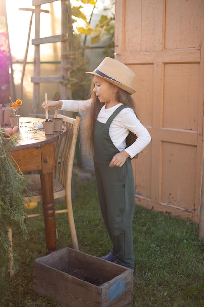 A vertical portrait of a cute funny blueeyed farmer girl in a hat with long hair and a green jumpsuit Horticulture Hobby Lifestyle