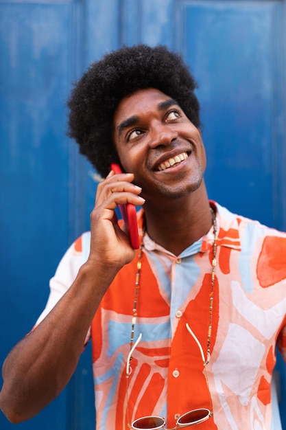 Vertical portrait of happy black man talking on the phone African American man with afro hairstyle using mobile phone in the street Lifestyle and technology concept