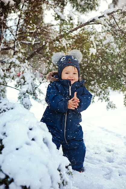 vertical portrait of a laughing baby boy on a snow near a fir tree