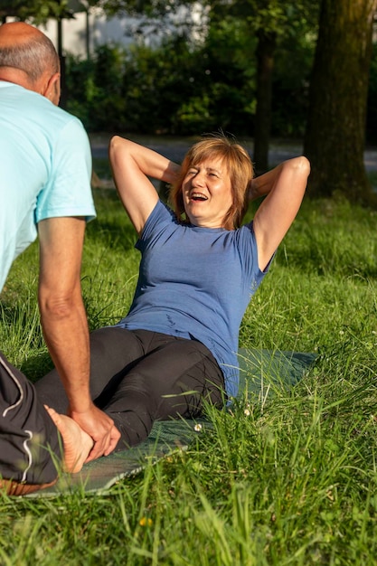 Vertical portrait of man and woman striving to do situps and have healthy lifestyle in the grass and nature