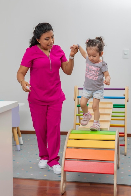 Vertical portrait of a nurse helping a girl walk through a wooden game