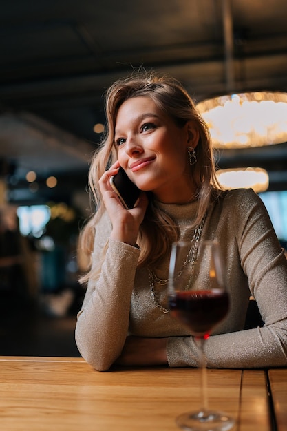 Vertical portrait of positive cute young woman talking on mobile phone with friend smiling discussing some latest news enjoying nice conversation