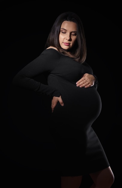 Vertical portrait of pregnant woman in black dress on black background with copy space