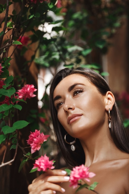 Vertical portrait of tanned caucasian woman standing near tropical flowers and gazing dreamily.