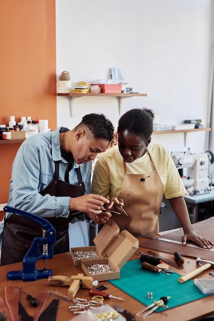 Vertical portrait of two female artisans in leatherworking shop creating handmade pieces together