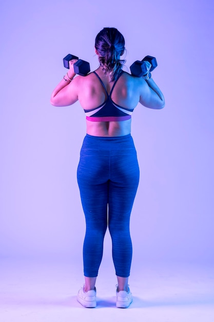 Vertical portrait of a woman from behind with two dumbbells on her shoulders