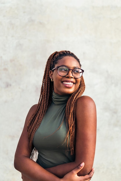 Vertical portrait of a young black woman with glasses smiling happy with a gray concrete wall in the background, concept of youth and racial diversity, copy space for text