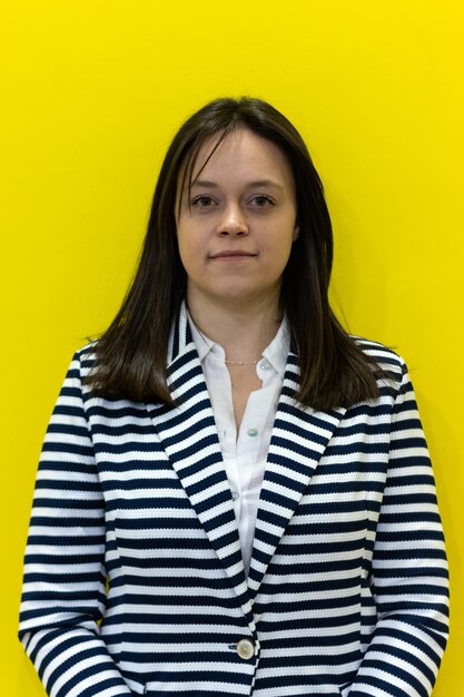 Vertical portrait of a young businesswoman smiling and looking at the camera on yellow background