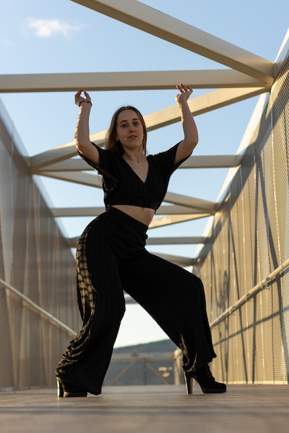 Vertical portrait of a young caucasian woman dancing urban dance at sunset on a bridge waacking dance style