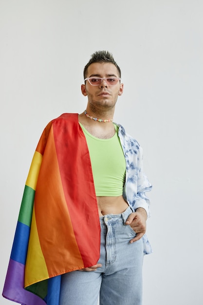 Photo vertical portrait of young gay man draped with pride flag against white background