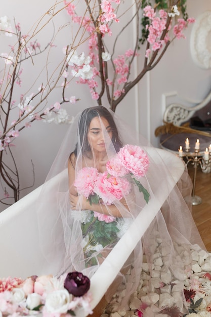 Vertical portrait of young girl holding bunch of flowers and sitting in a bathtub High quality photo