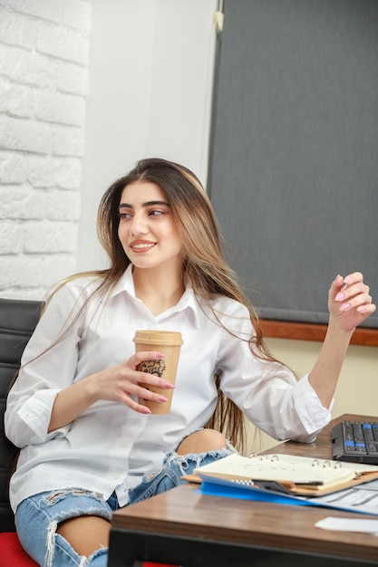 Vertical portrait of a young lady holding cup of coffee and looking away High quality photo