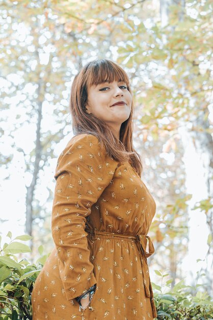 Vertical portrait of a young red head woman smiling happy to camera while wearing modern and trendy dress. Self confidence and womanhood attitude concepts, feminism and woman pride