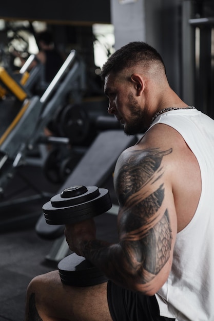 Vertical rear view cropped shot of a tattooed bodybuilder resting with dumbbells in his hands