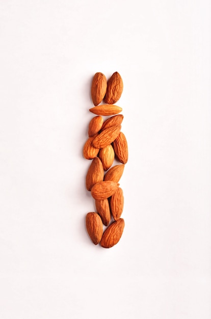 A vertical row of dry raw almond nuts on a studio white background. Food diet composition top of the view.