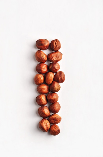 A vertical row of dry raw hazelnuts on a studio white background. Food vegetarian composition top of the view.