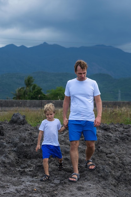 VERTICAL Serious Father son or adult younger brother walk together look for adventure Cloudy sky before rain mountain background Man talk hold boy by hand attentive look Natural science education