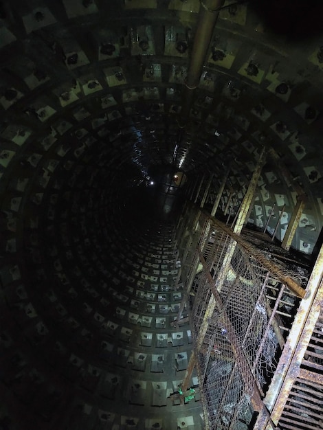 A vertical shaft of a sewage collector with a rusty ladder to the top View from below