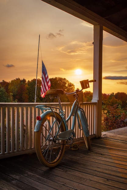 Vertical shot of a bike outside of a wooden house by the United State flag against the sunset sky